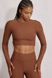 חולצת קרופ שרוול ארוך מהקולקציה בעיצובה של אדל בספלוב, בשילוב של חיתוכי לייזר, חיתוך לב בפריט ללא שכבה פנימית, מקום לאגודל, גוון חום.