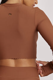 חולצת קרופ שרוול ארוך מהקולקציה בעיצובה של אדל בספלוב, בשילוב של חיתוכי לייזר, חיתוך לב בפריט ללא שכבה פנימית, מקום לאגודל, גוון חום.